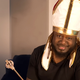 T-Pain wearing a pope hat and cepter while looking down the barrel of a camera lens